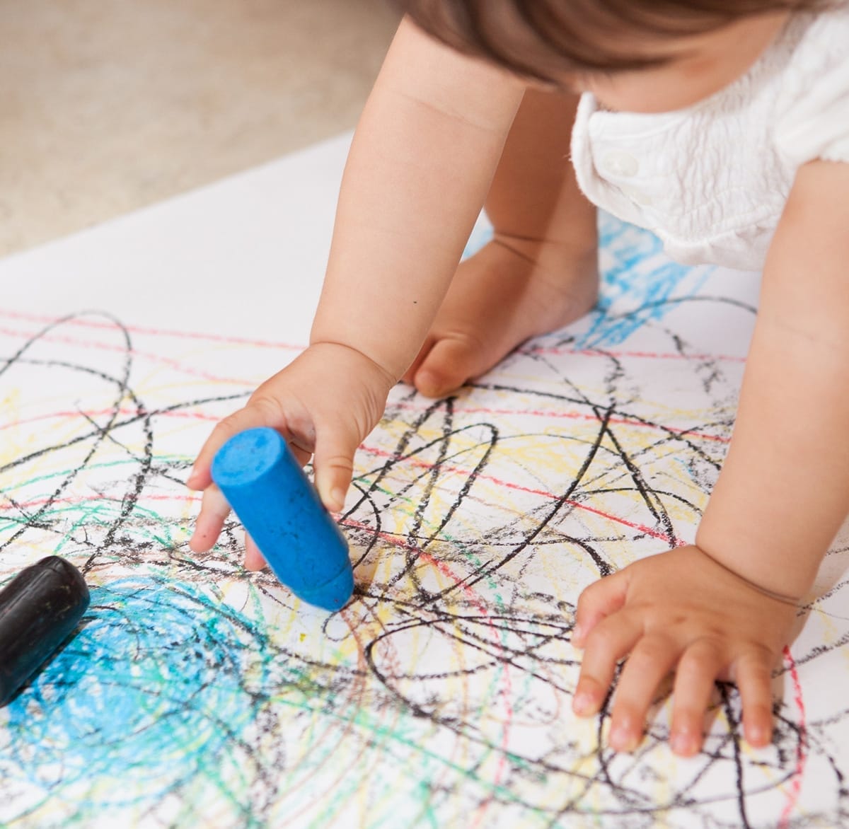 Preschooler draws on white paper sitting on floor
