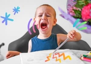 A 2-year-old child draws with colored pencils in an album and screams.