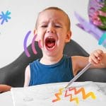 A 2-year-old child draws with colored pencils in an album and screams.