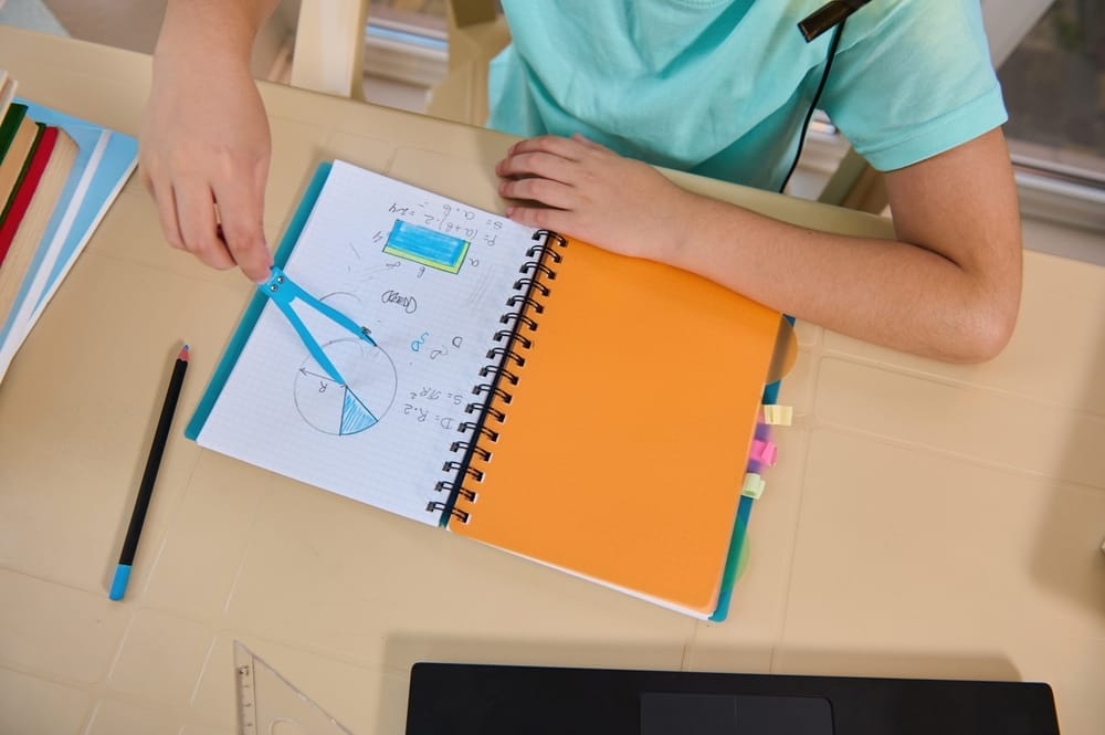 Overhead view of the hand of schoolboy holding compass drawing geometry